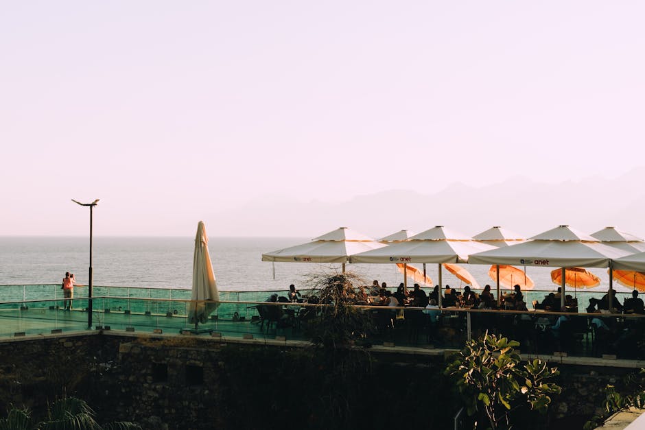 Outdoor restaurant terrace with ocean view, parasols, and people dining at sunset