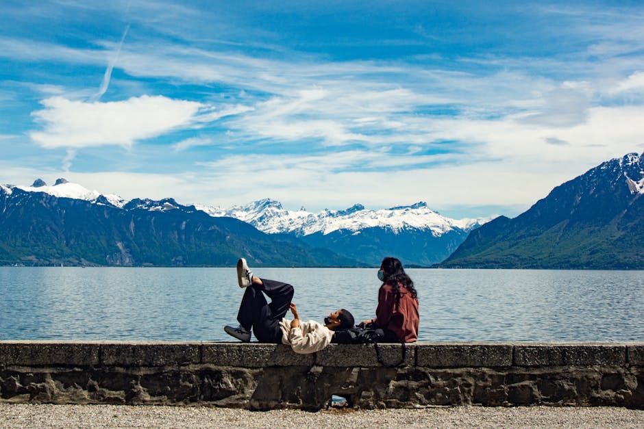 A couple enjoys a serene vacation by a snowcapped mountain lake under a bright blue sky