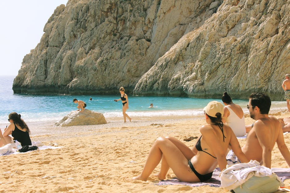 People enjoying a sunny day at a picturesque beach with rocky cliffs and clear blue water