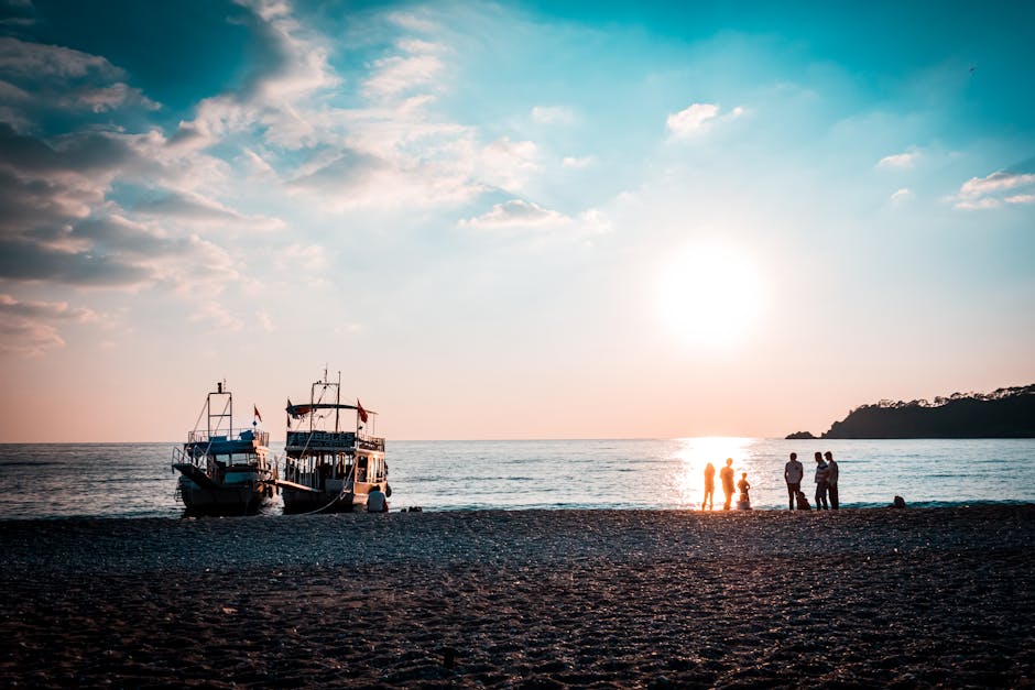 Silhouettes of people by boats on a sunlit beach, creating a tranquil sunset scene